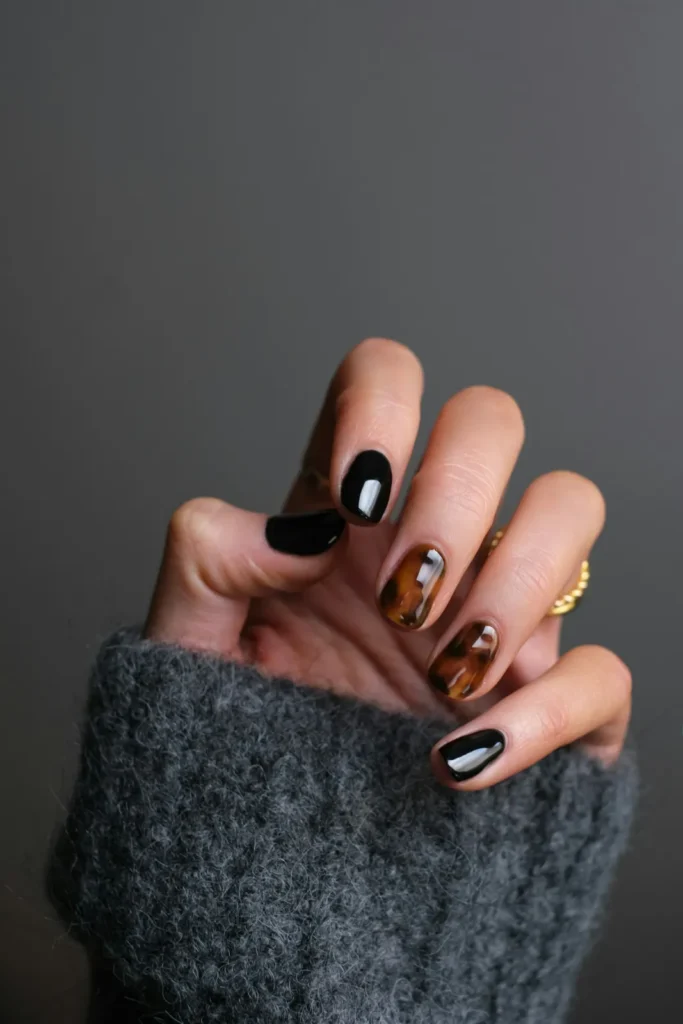 Black and tortoiseshell nails on a grey knit sleeve