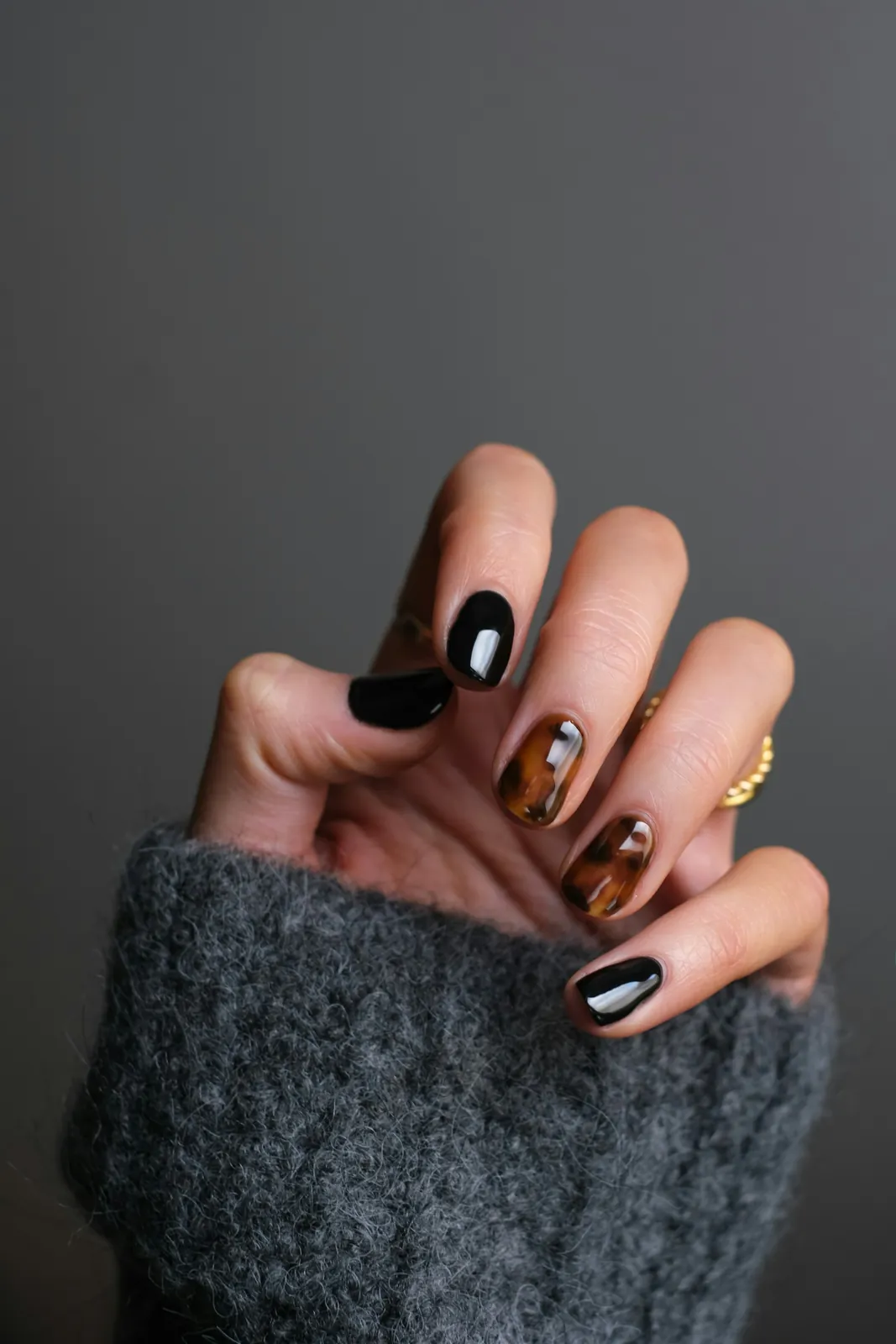 Black and tortoiseshell nails on a grey knit sleeve