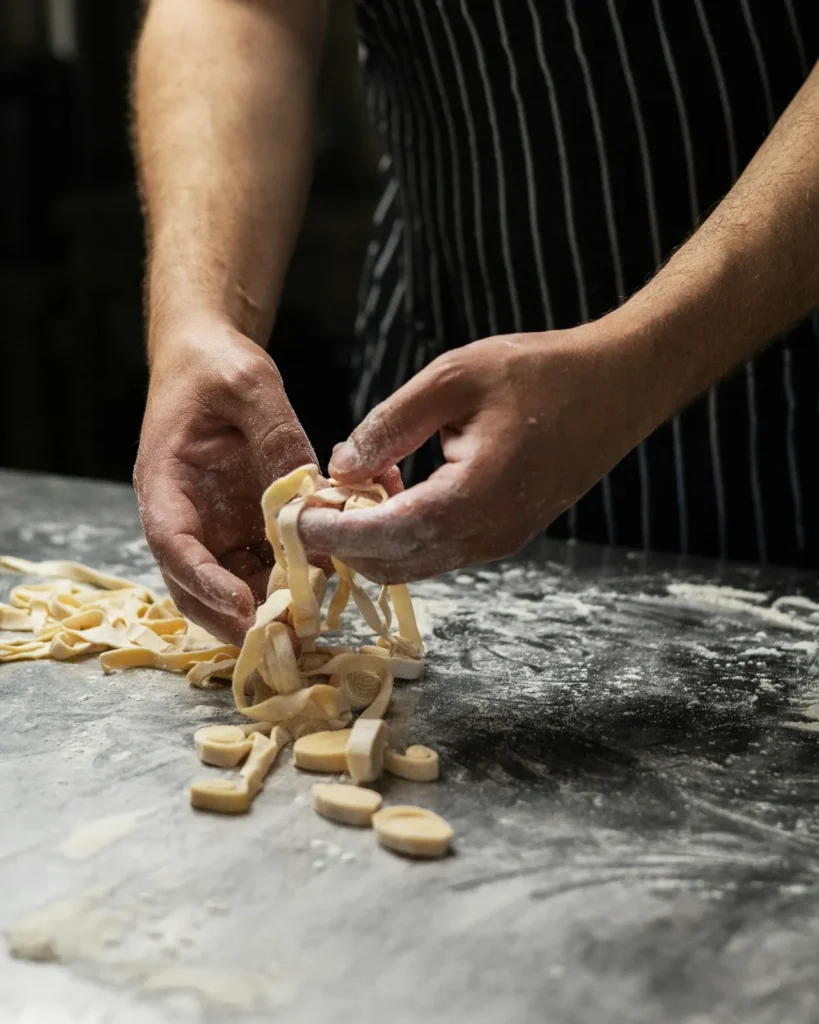 Hands shaping fresh pasta on a floured counter