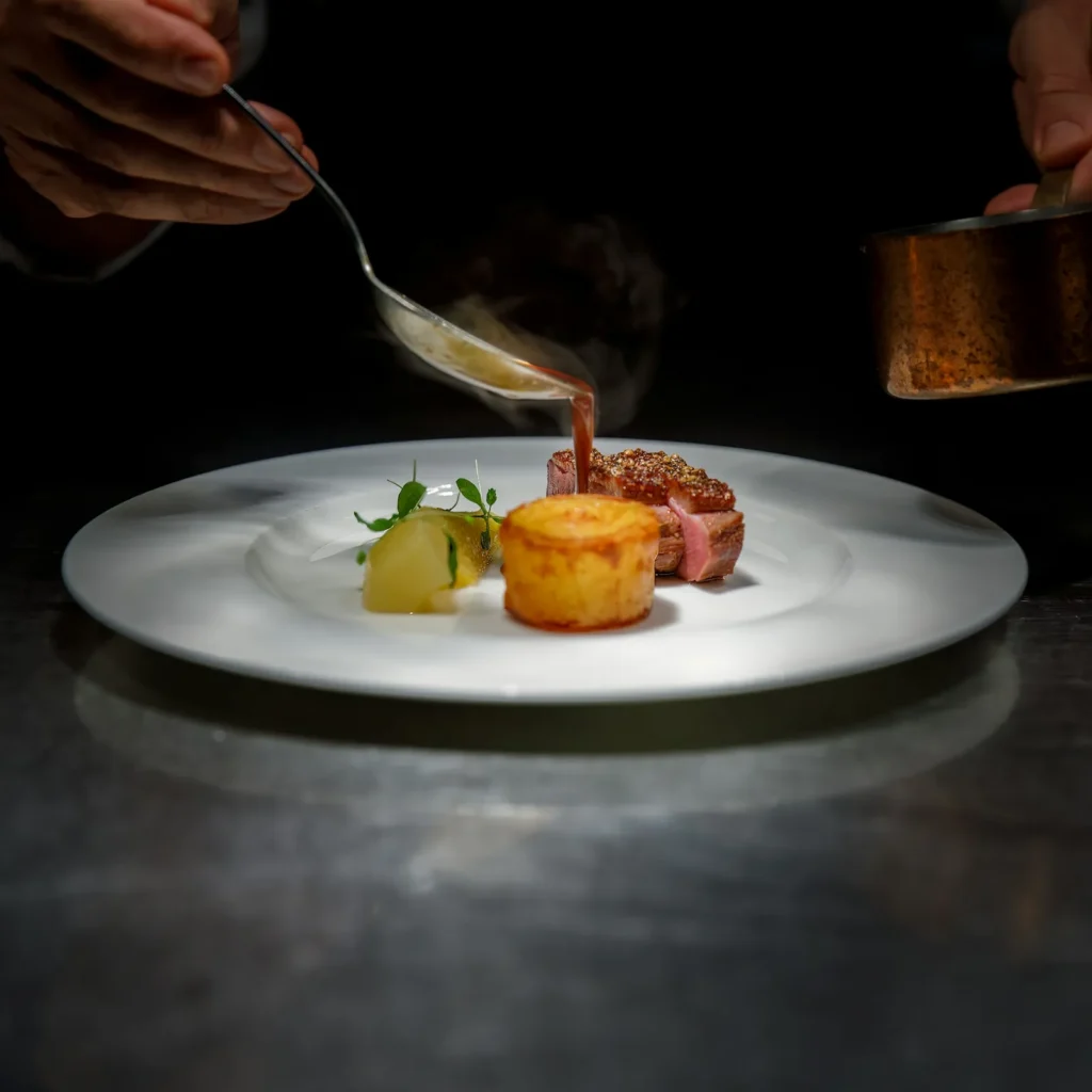 Chef spooning sauce over a plated course