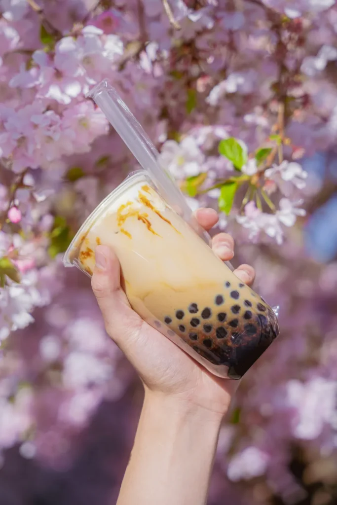 Hand holding a milk tea with pearls under blossoms