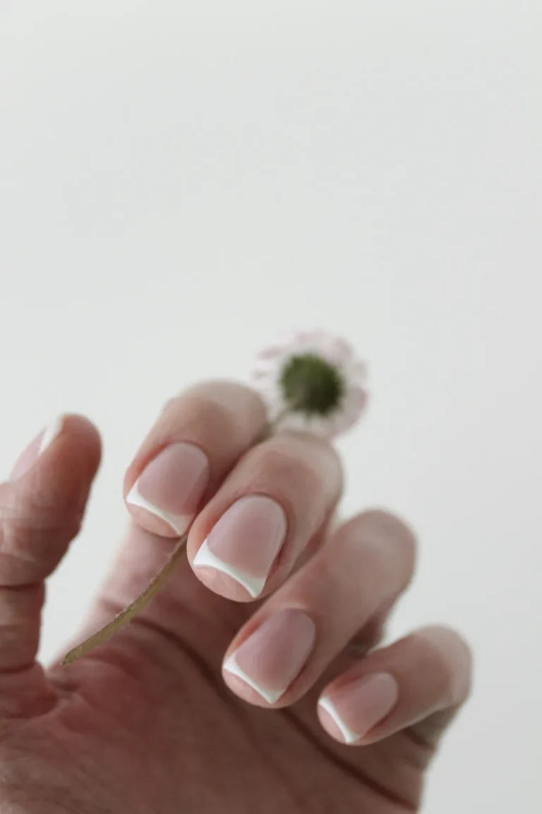 Classic French manicure holding a daisy
