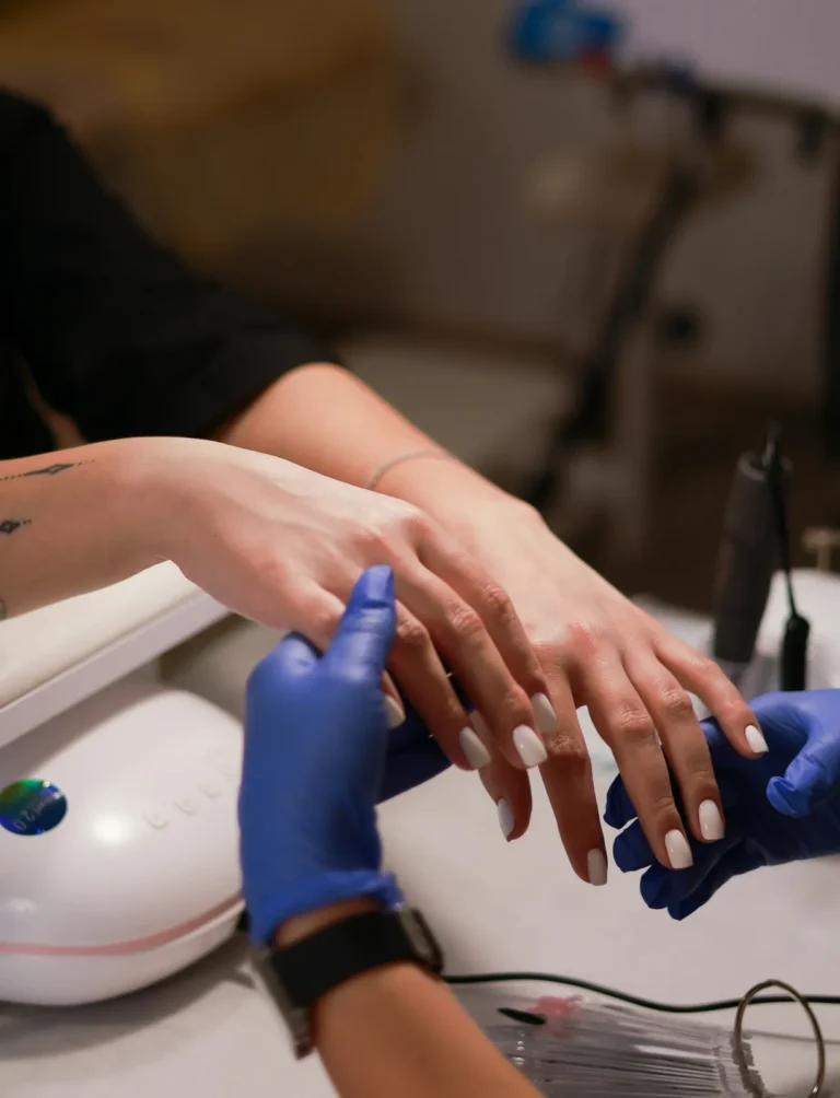 Nail technician in blue gloves holding a client's hand