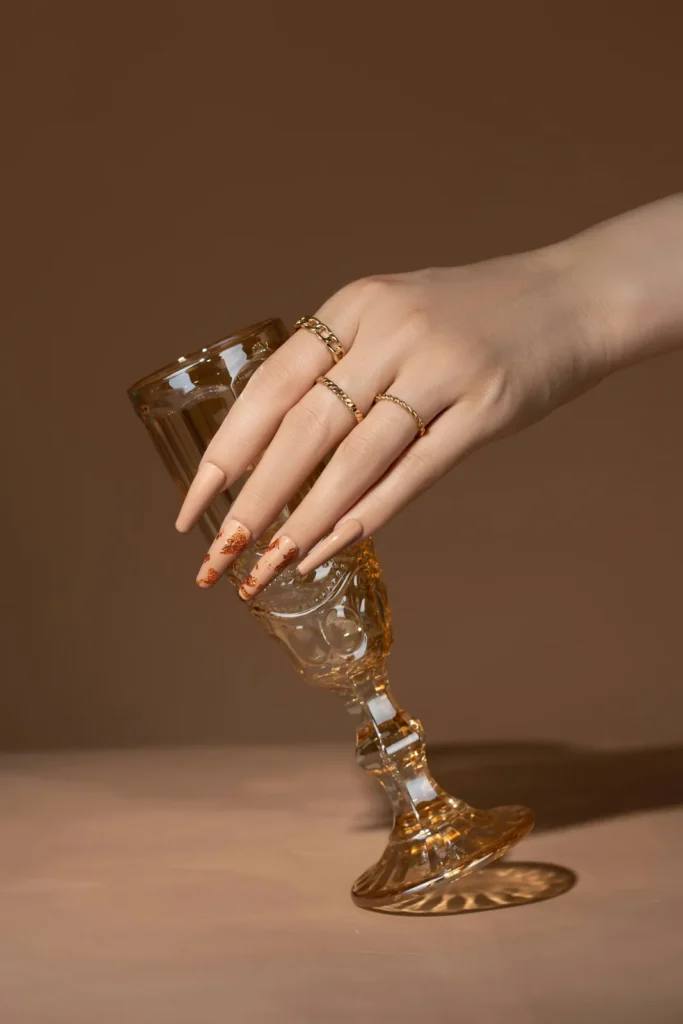 Long nude nails and gold rings around a champagne glass