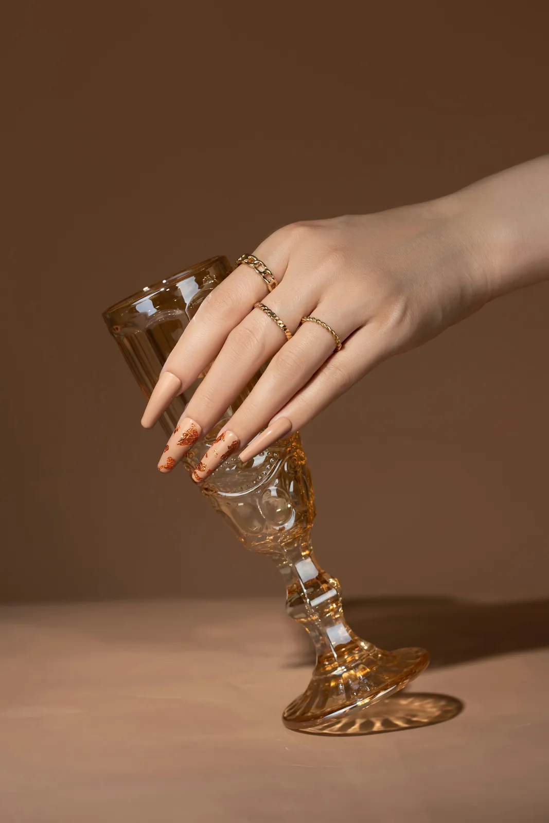 Long nude nails and gold rings around a champagne glass