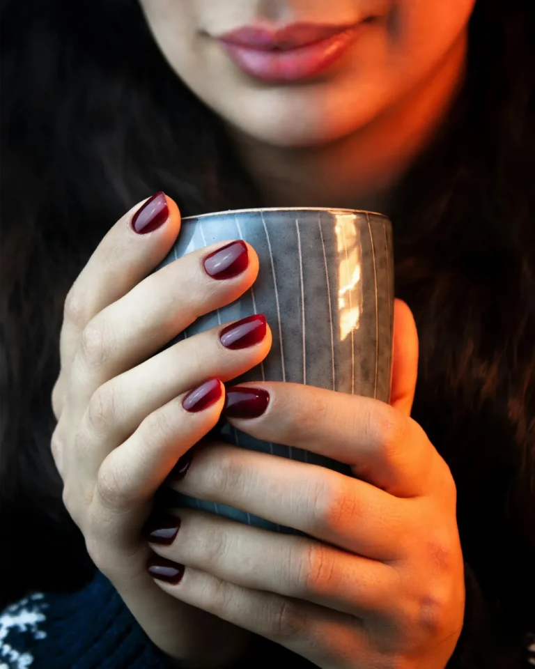 Deep red nails holding a ceramic cup