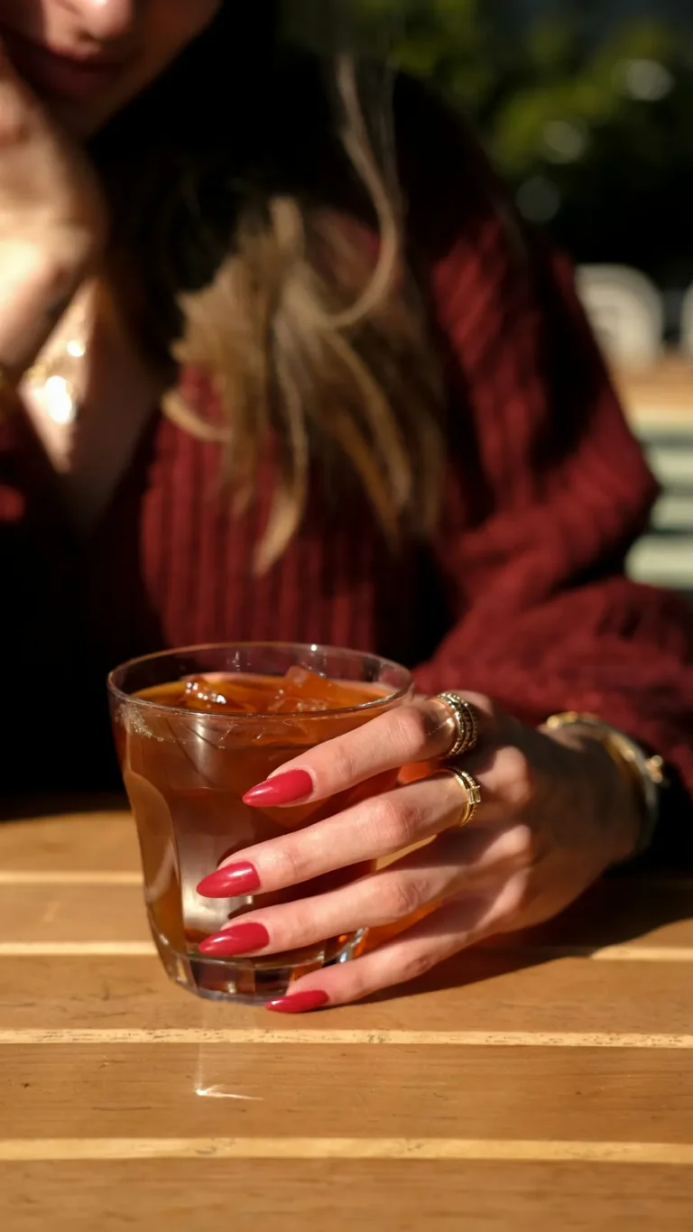 Red nails and gold rings around an iced drink