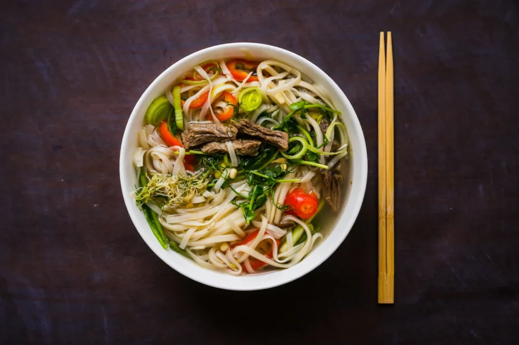 Bowl of pho with herbs and chopsticks on a dark table