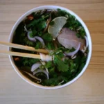 Chopsticks lifting noodles from a bowl of pho