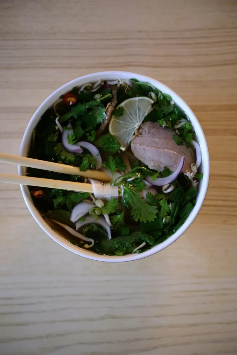 Chopsticks lifting noodles from a bowl of pho