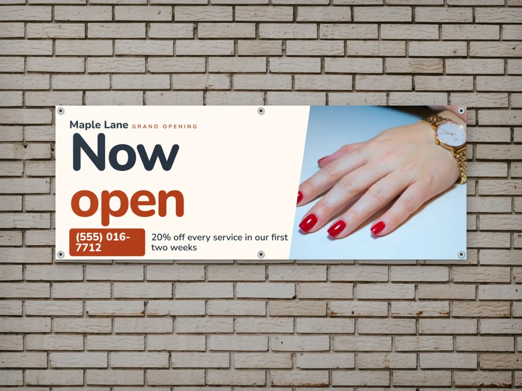 A grand opening vinyl banner for a nail salon on a brick wall
