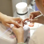 Nail technician working on a client's nails beside a gel lamp