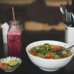 A bowl of pho and a drink on a restaurant table