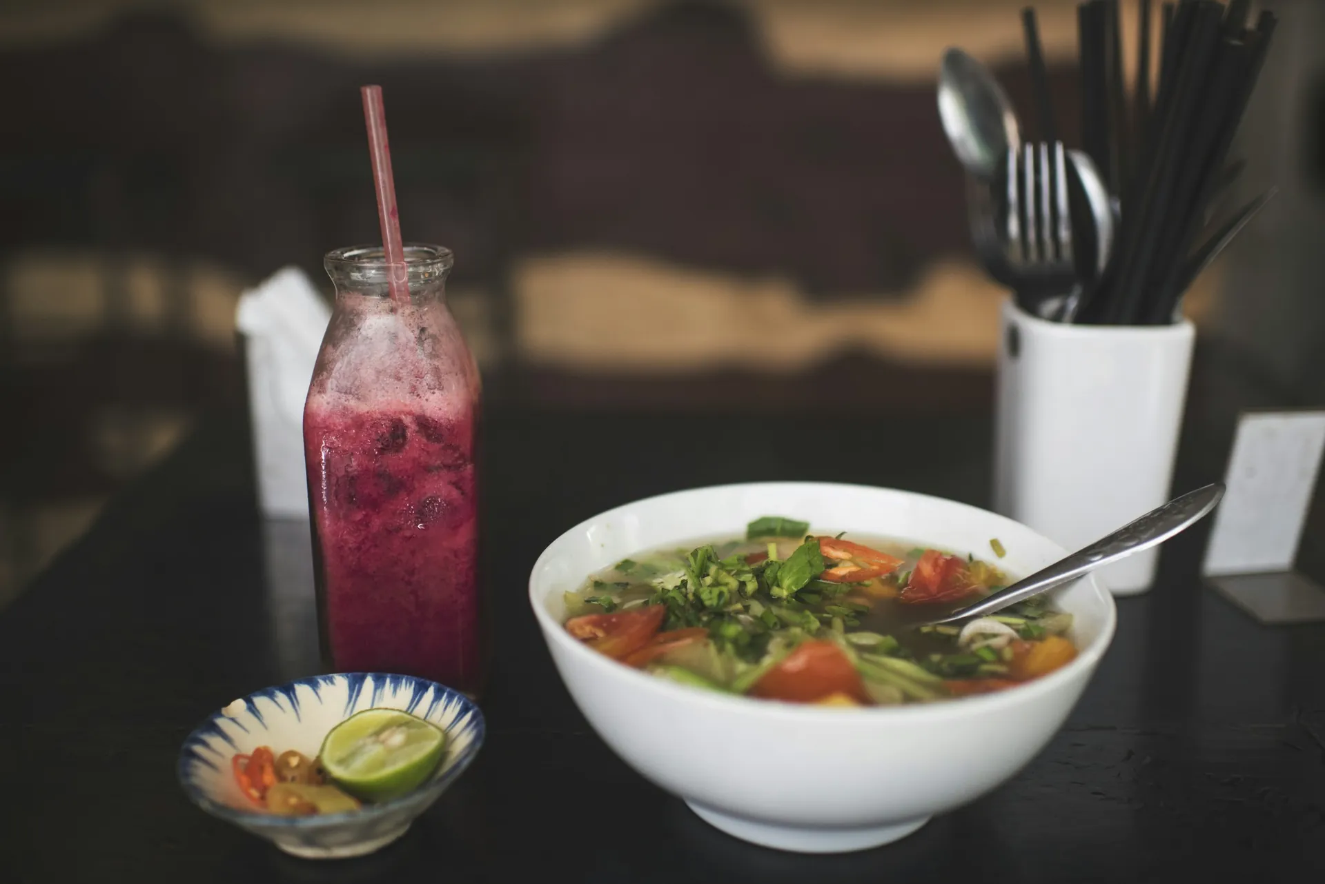 A bowl of pho and a drink on a restaurant table